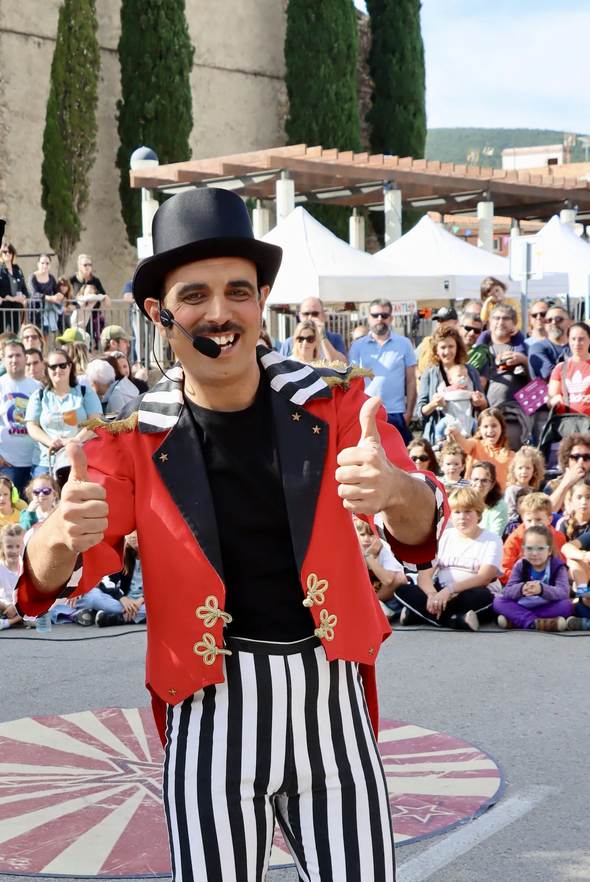 Un pallasso amb barret de copa saluda la canalla asseguda al carrer