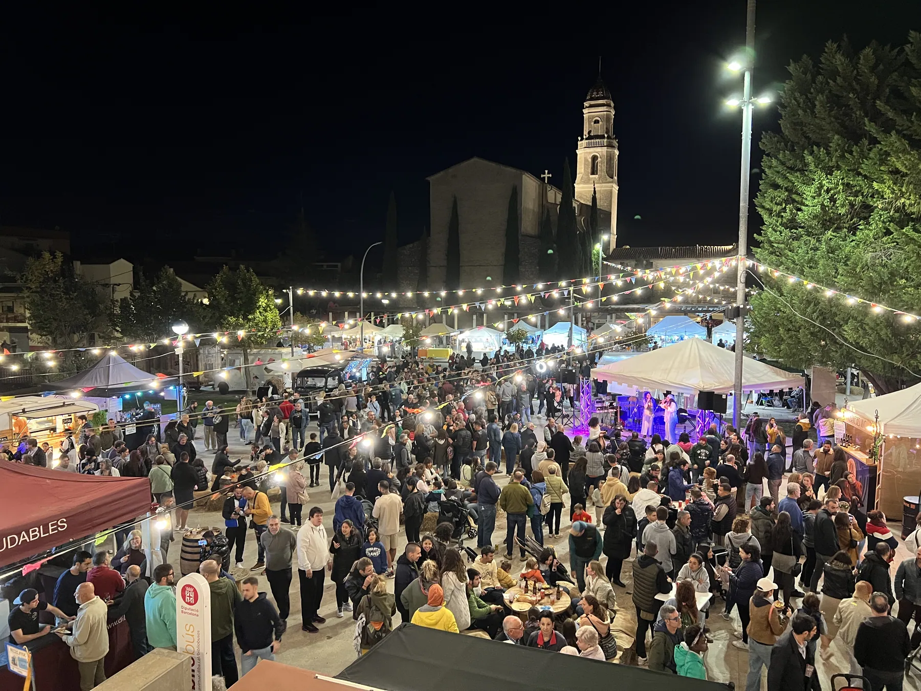 La Plaça Lluís Companys plena de gent sota les garlandes de llums, amb el campanar al fons